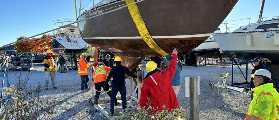 Haulout crew in hard hats guiding a sailboat in the slings