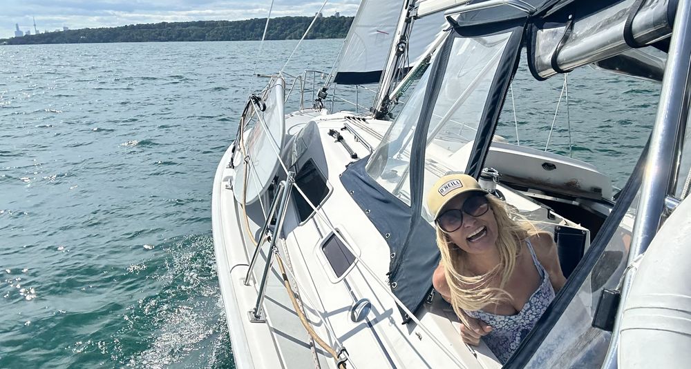 A smiling sailor in the cockpit of a sailboat under way