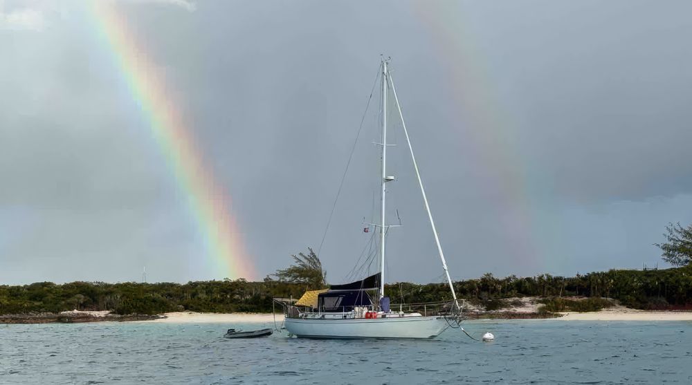 A sailboat at anchor under a double rainbow