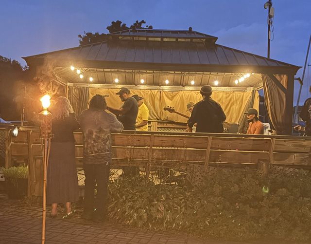 A dock gazebo lit with string lights and tiki torches at dusk